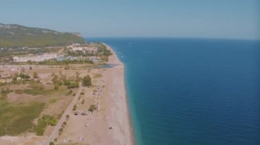 Kıyı şeridinin en üst manzarası. Deniz ve kumlu sahil. Güneşli bir gün. Denizde iskele. Kumsaldaki güneş pansiyonları ve şemsiyeler. Yüksek kalite 4k görüntü