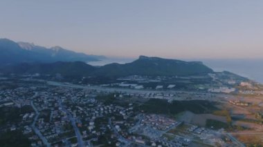 Gün batımı, bir dağ manzarasının arka planına karşı. Deniz kenarındaki turist kasabası. Deniz manzaralı bir drone görüntüsü. Yüksek kalite 4k görüntü