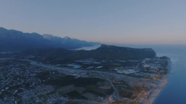 Deniz kenarındaki bir turist kasabasının insansız hava aracı görüntüleri. Gün batımı, bir dağ manzarasının arka planına karşı. Yüksek kalite 4k görüntü