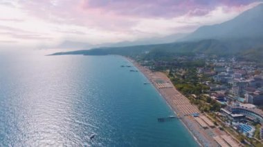 Deniz kenarındaki bir turist kasabasının insansız hava aracı görüntüleri. Gün batımı, bir dağ manzarasının arka planına karşı. Yüksek kalite 4k görüntü
