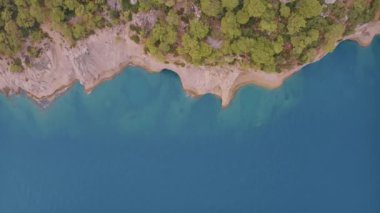 Yeşil ağaçlarla kaplı kayalık bir kıyı manzarası. Kayadaki mağara. Mavi berrak su. Güzel deniz manzarası. İHA video görüntüleri. Yüksek kalite 4k görüntü