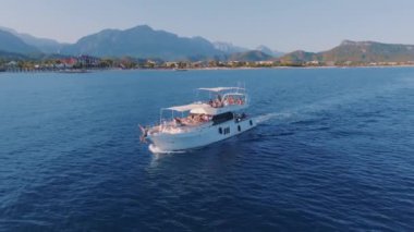 Bir adam yatın pruvasında oturuyor. Denizde yattı. Gemide insanlar var. Turizm ve eğlence. Deniz Burnu. Bir İHA 'nın hava görüntüsü. Yüksek kalite 4k görüntü