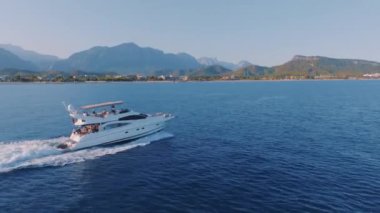 Sakin mavi denizde turist yatı hızla ilerliyor. Gün batımı. Deniz Burnu. Arka planda dağlar. Hava aracı video görüntüleri. Yüksek kalite 4k görüntü