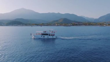 Yat, bir dağ manzarasının arka planına karşı mavi denizde hızla ilerliyor. Deniz Burnu. İHA video görüntüleri. Yüksek kalite 4k görüntü