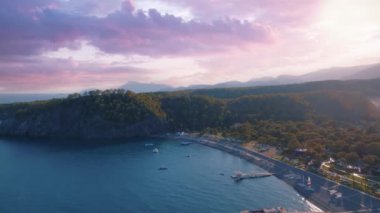 Hava aracı video görüntüleri. Gün batımında deniz manzarası. Kıyıda mavi deniz ve yeşil ağaçlar. Arka planda dağlar. Yüksek kalite 4k görüntü