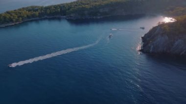 Yat sakin mavi denizde hızlı bir şekilde ilerliyor. Gün batımı. Deniz Burnu. Arka planda dağlar. Hava aracı video görüntüleri. Yüksek kalite 4k görüntü