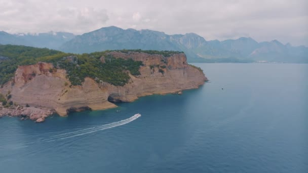 海の大きな岩の島の上を飛行します ボートは航行中です 山を背景に 空中ドローン映像 高品質4K映像 — ストック動画