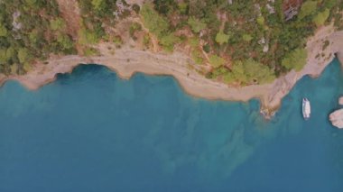 Yeşil ağaçlarla kaplı kayalık bir kıyı manzarası. Kayadaki mağara. Tekne kıyıya yakın. İHA video görüntüleri. Yüksek kalite 4k görüntü