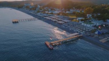 Hava aracı video görüntüleri gün batımında deniz manzarası. İskele. Kumsal, şemsiyeler, dinlenme yerleri. Arka planda dağlar. Yüksek kalite 4k görüntü