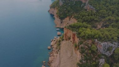 Yeşil ağaçlarla kaplı kayalık bir kıyı manzarası. Kayadaki mağara. Mavi berrak su. Güzel deniz manzarası. İHA video görüntüleri. Yüksek kalite 4k görüntü