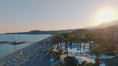 Gün batımında deniz manzaralı bir hava aracı. İskele. Kumsal, şemsiyeler, güneşlik, palmiye. Arka planda dağlar. Yüksek kalite fotoğraf