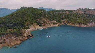 Yeşil ağaçlarla kaplı kayalık bir kıyı manzarası. Kayadaki mağara. Mavi berrak su. Deniz Burnu. Yüksek kalite fotoğraf