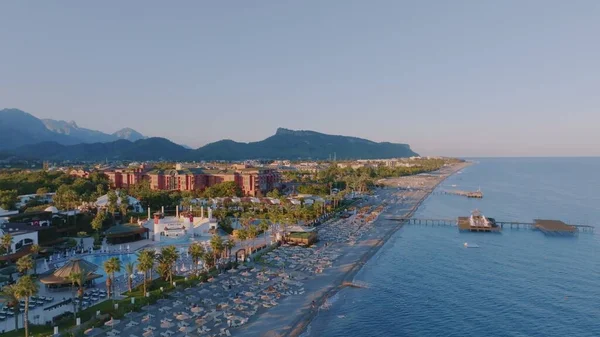 Gün batımında deniz manzarası. İskele. Kumsal, şemsiyeler, güneşlik, palmiye. Arka planda dağlar. Yüksek kalite fotoğraf