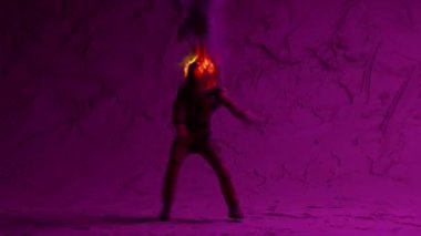 An astronaut with a burning head dances a modern dancing in front of purple illuminated lights. Abstract background. High quality 4k footage