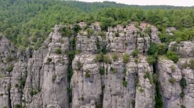 Uçsuz bucaksız, kayalık uçurumlar, yemyeşil ormanlar ve tepede bir grup insan.