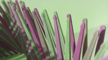 Yeşil, pembe ve mor tonlarda parlak ahşap çubuklar açık yeşil arka planda spiral bir düzende dizilmiştir..