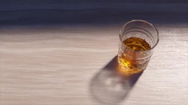 Pencereden süzülen güneş ışığı bir bardak viskiyi aydınlatır, sıcak bir parıltı yaratır ve pürüzsüz ahşap bir masa üzerinde karmaşık gölgeler bırakır, sıcak atmosferi güçlendirir.