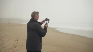 Sahilde telefon dinamosu kullanarak çekim yapan yaşlı beyaz bir adam. Zoom atışı. Yüksek kalite 4K görüntü