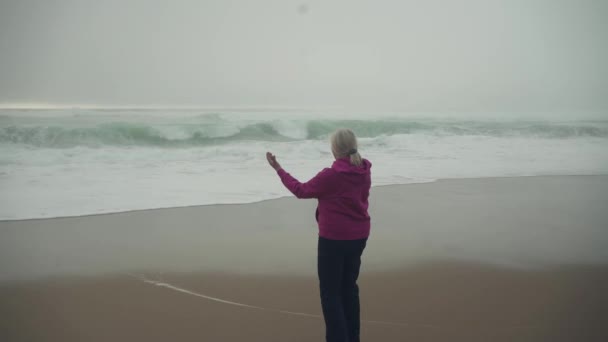 Mulher Branca Caucasiana Idosa Com Capuz Roxo Meditando Junto Oceano — Vídeo de Stock