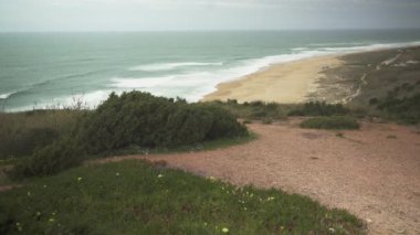  Nazare, Portekiz 'de bulutlu bir günde geniş bir kıyı manzarası. Uzun dalgalar, mavi gökyüzü, kumlu sahil. Yüksek kalite 4K görüntü