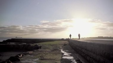 Gün batımında iskelede yürüyen insanların siluetleri. Estoril, Cascais, Portekiz 'deki Atlantik sahili plajı. Yüksek kalite 4K görüntü