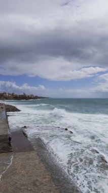 Estoril sahilindeki taş iskelede dalgalar süzülüyor. Hava görüntüsü. Uçan bir İHA atışı. Yüksek kalite 4k.