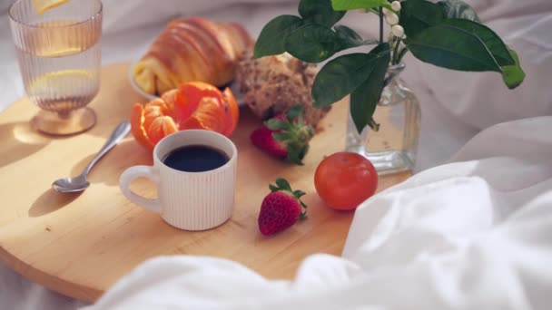 白いリネンが付いているベッドの丸い木の皿のコーヒー タンジェリンおよびクロワッサンのカップ 横4K映像について — ストック動画