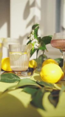 Su ve limonlu bardaklar. Güneşli bir günde limon ve çiçeklerle süslenmiş bir masada sağlıklı içecekleri tazelemek. Yüksek kalite 4K görüntü