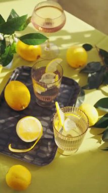 Su ve limonlu bardaklar. Güneşli bir günde limon ve çiçeklerle süslenmiş bir masada sağlıklı içecekleri tazelemek. Yüksek kalite 4K görüntü