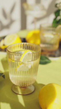Su ve limonlu bardaklar. Güneşli bir günde limon ve çiçeklerle süslenmiş bir masada sağlıklı içecekleri tazelemek. Yüksek kalite 4K görüntü