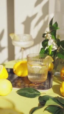 Su ve limonlu bardaklar. Güneşli bir günde limon ve çiçeklerle süslenmiş bir masada sağlıklı içecekleri tazelemek. Yüksek kalite 4K görüntü