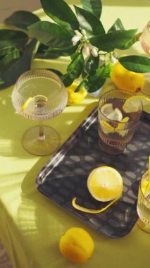 Su ve limonlu bardaklar. Güneşli bir günde limon ve çiçeklerle süslenmiş bir masada sağlıklı içecekleri tazelemek. Yüksek kalite 4K görüntü