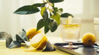 Su ve limonlu bardaklar. Güneşli bir günde limon ve çiçeklerle süslenmiş bir masada sağlıklı içecekleri tazelemek. Yüksek kalite 4K görüntü