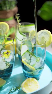 Bir bardağa eritilmiş su doldurmak ve bir pipet koymak. Mavi tepside salatalık ve limonlu detoks suyu. Yaz ev yapımı kokteyller. Dikey video. Yüksek kalite 4K görüntü. Döndürme hareketi