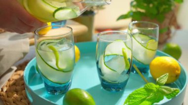 Salatalık ve limon bardaklara detoks suyu dökülüyor. Yaz ev yapımı kokteyller. Yüksek kalite 4K görüntü. Kamera hareketi döndürülüyor