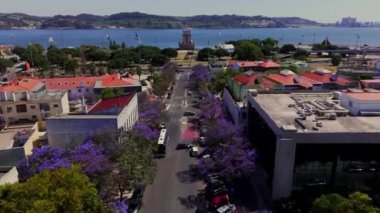 Bulvarın havadan çekimleri, çiçek açan jakaranda ağaçları ve arka planda Belem Kulesi ve Tagus Nehri ile sınırlıydı. Avenida da Torre de Belem, Lizbon, Portekiz. Yüksek kalite 4k görüntü