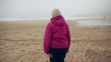 Portekiz, Cascais 'deki Praia do Guincho kumsalında okyanus manzarasının keyfini çıkaran son sınıf bir kadının arka çekimi. Yüksek kalite 4k görüntü