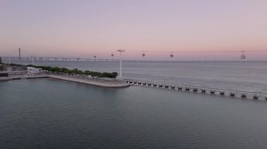 Tagus Nehri ve ikonik Vasco da Gama Köprüsü ile Alacakaranlık Saati boyunca sahil boyunca uzanan teleferiklerin yer aldığı, Lisbons Milletler Parkının parkı das Nacoes 'un hava görüntüsü..