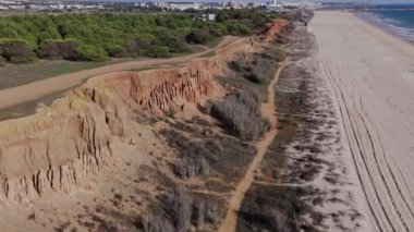 Falesia Sahili üzerinde uçan İHA dalgaları, kumlu kumsallar ve terracotta kayalarını ortaya çıkarıyor. Vilamoura, Algarve. 