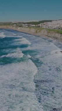 Kumlu sahil boyunca uçan ve dalgalı hava aracı Ericeira köyünü ortaya çıkarıyor. Dikey video. Yüksek kalite 4k görüntü