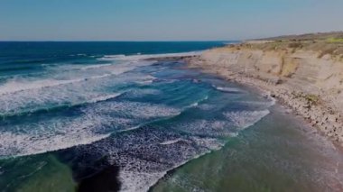 Kumlu sahil boyunca uçan ve dalgalı hava aracı Ericeira köyünü ortaya çıkarıyor. Dikey video. Yüksek kalite 4k görüntü