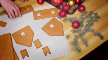  Dinamik kamera hareketleriyle zencefilli bir evi adım adım birleştirme süreci. Festivalde kırmızı Noel süsleri, çam dalları ve tahta bir masa üzerindeki mevsimlik dekorlar yer alıyor..