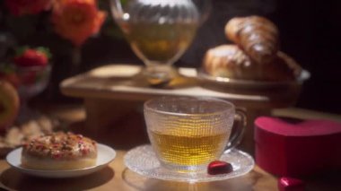 Bir yemek takımının detaylı bir görüntüsü: taze kruvasanlar, renkli şekerli çörekler ve bir çay fincanı. Sevgililer Günü ve romantik tatiller için rahat bir ortam.