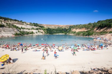 BESENOVO, SERBIA - 3 Temmuz 2022: Fruska gora dağları, Voyvodina, Sırbistan 'da Besenovo Gölü veya Besenovo Gölü önünde güneşlenen kalabalık bir plajın panoraması