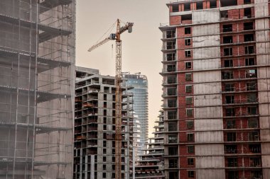 Bir emlak geliştirme alanında inşaat iskeleleri, beton ve beton cepheleri ve vinçleri olan gökdelen kulelerinden oluşan bir bina kompleksinin panoraması.