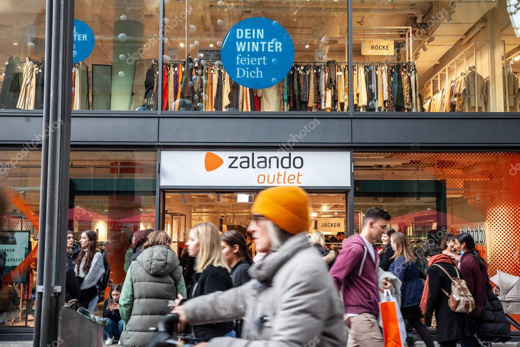 COLOGNE, GERMANY - NOVEMBER 12, 2022: Selective blur on a Zalando logo on their outlet store of Cologne with blurred clients passing by. Zalado is an online german fashion retailer