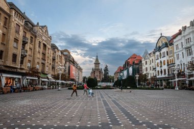 TIMISOARA, ROMANIA - SEPTEMBER 16, 2022: İkonik Zafer Meydanı (Piata Victoriei), Metropolitan Katedrali (Katedral Mitropolitana), Timisoara 'nın ana meydanı ve simgesi bir aile, anne baba ve kızıyla birlikte seçici bulanıklık.