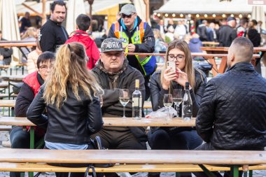 SZEGED, HUNGARY 19 Eylül 2022: Szeged 'de akıllı telefonuyla Macar beyaz şarabı içen bir aile, baba, anne ve kızı hakkında seçici bulanıklık. Macaristan büyük bir alkol ve şarap üreticisi..