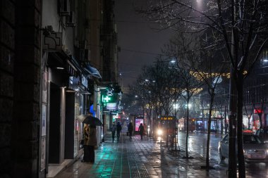 BELGRAD, SERBIA - 11 Aralık 2021: Yağmurun altında şemsiyeli seçici bulanık insanlar, Sırplar, Belgrad şehir merkezinin bir caddesi olan Kralja Milana 'nın caddesinde bir kış akşamı Sırp başkentinde yürüyorlar