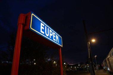 Eupen tren istasyonundaki bir levhada seçici bulanıklık, gece aydınlanması, şehrin adını gösteriyor. Eupen, Belçika 'nın Belçika eyaletinde yer alan bir şehirdir..